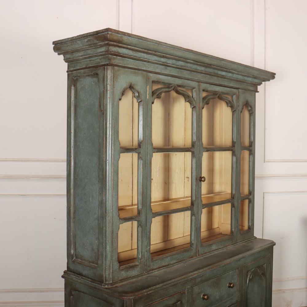 A two-part blue-green painted timber dresser featuring an upper glazed cabinet with gothic arch doors and a lower base fitted with drawers and cupboard doors. View XII