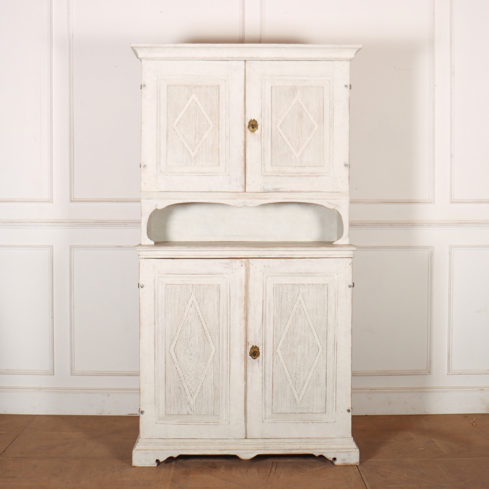 A two-tier Swedish painted wooden cabinet featuring distressed off-white paint, carved diamond geometric panels on four doors, and central brass escutcheons.