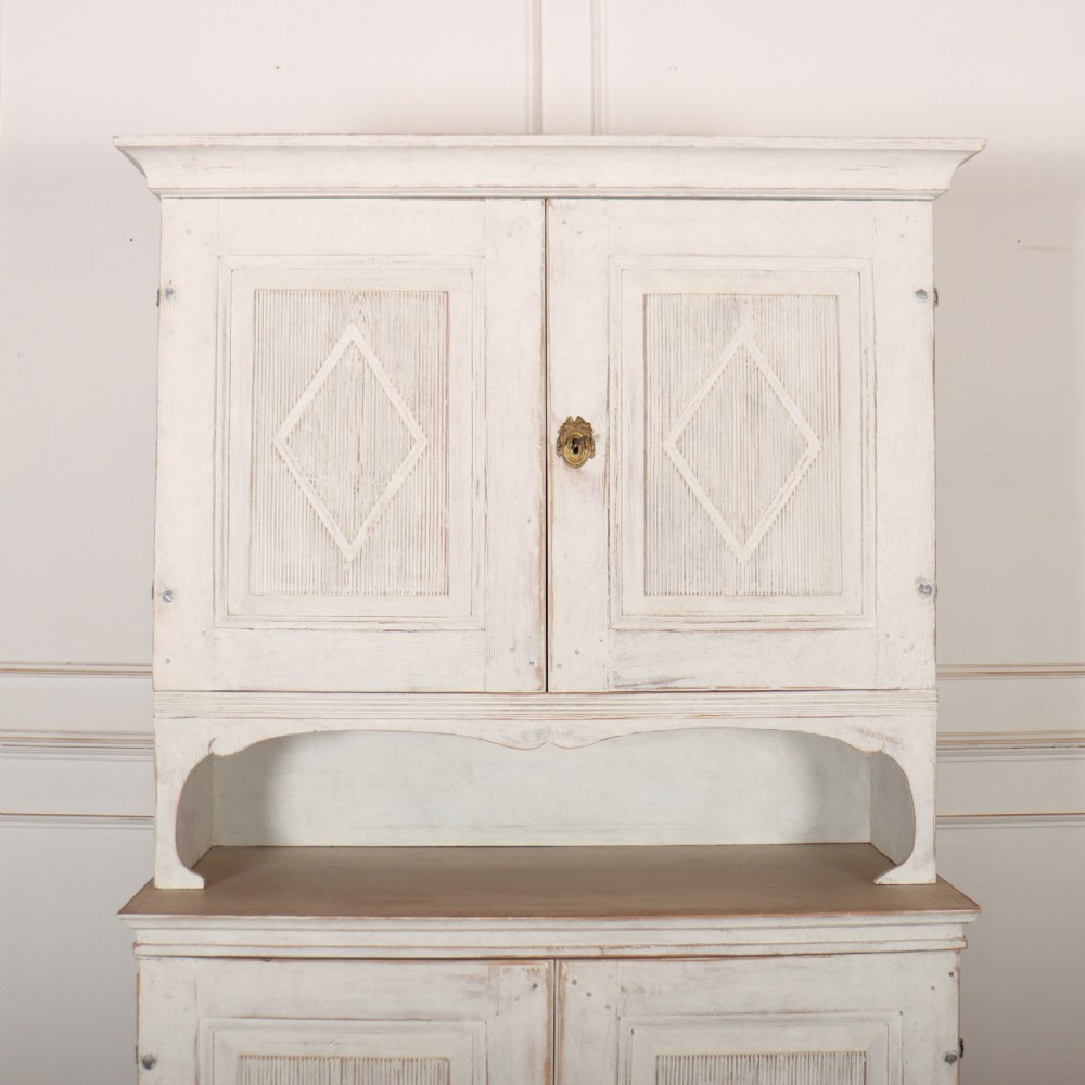 A two-tier Swedish painted wooden cabinet featuring distressed off-white paint, carved diamond geometric panels on four doors, and central brass escutcheons. View II