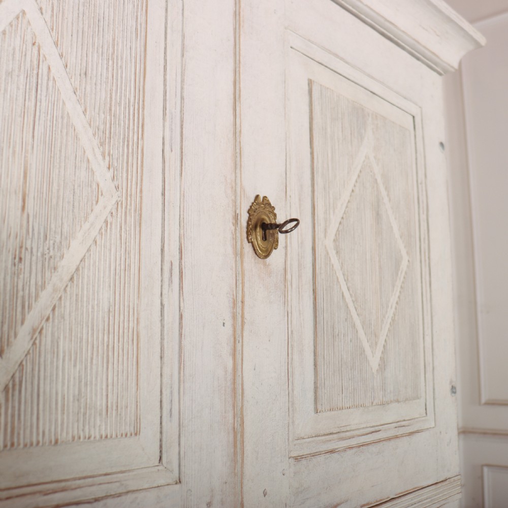 A two-tier Swedish painted wooden cabinet featuring distressed off-white paint, carved diamond geometric panels on four doors, and central brass escutcheons. View V