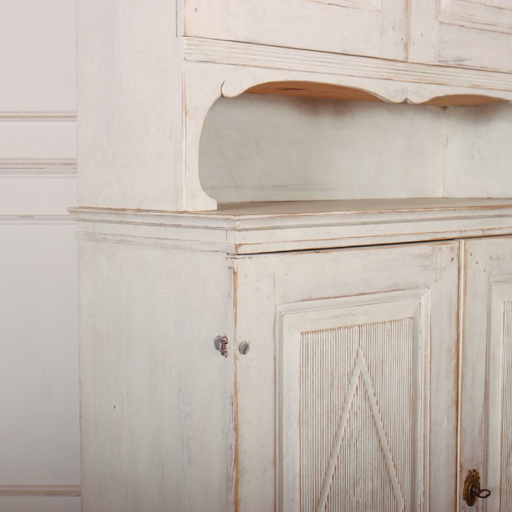 A two-tier Swedish painted wooden cabinet featuring distressed off-white paint, carved diamond geometric panels on four doors, and central brass escutcheons. View VIII