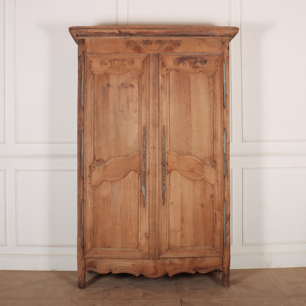 An 18th-century French provincial bleached oak armoire featuring two carved panel doors, long vertical iron hinges, and a moulded cornice.