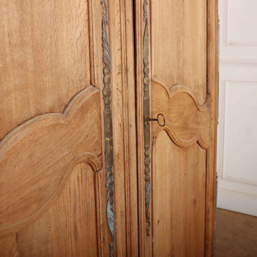 An 18th-century French provincial bleached oak armoire featuring two carved panel doors, long vertical iron hinges, and a moulded cornice. View IV