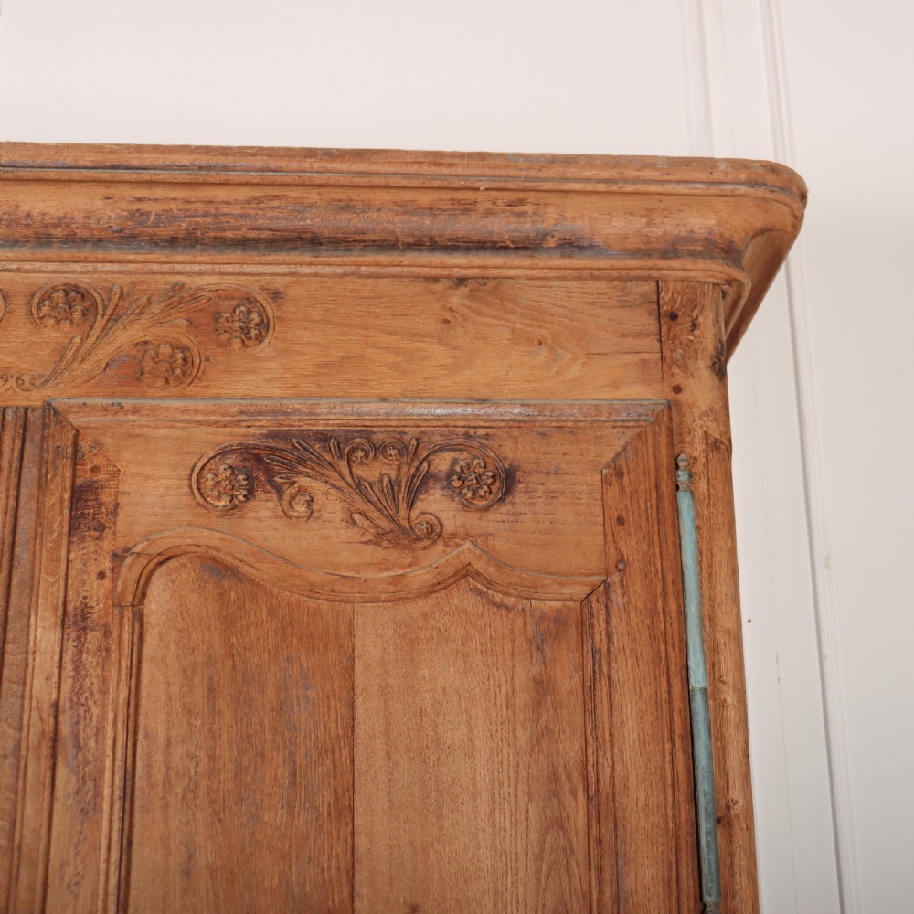 An 18th-century French provincial bleached oak armoire featuring two carved panel doors, long vertical iron hinges, and a moulded cornice. View VI