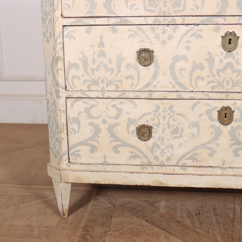 A Swedish painted pine commode featuring three drawers decorated with off-white and grey damask pattern paintwork, brass escutcheons, and tapered square legs. View III