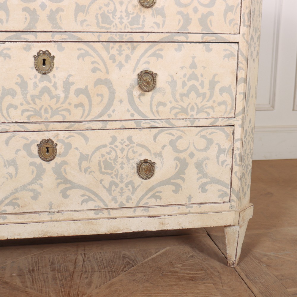 A Swedish painted pine commode featuring three drawers decorated with off-white and grey damask pattern paintwork, brass escutcheons, and tapered square legs. View VI
