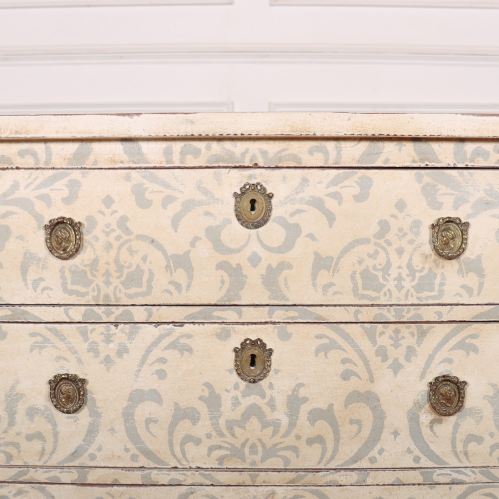 A Swedish painted pine commode featuring three drawers decorated with off-white and grey damask pattern paintwork, brass escutcheons, and tapered square legs. View VII