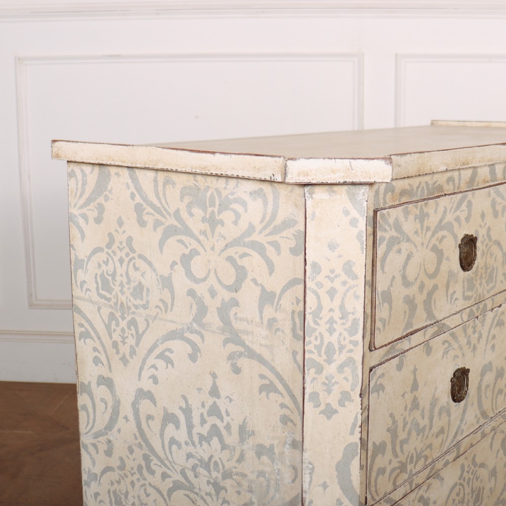 A Swedish painted pine commode featuring three drawers decorated with off-white and grey damask pattern paintwork, brass escutcheons, and tapered square legs. View IX