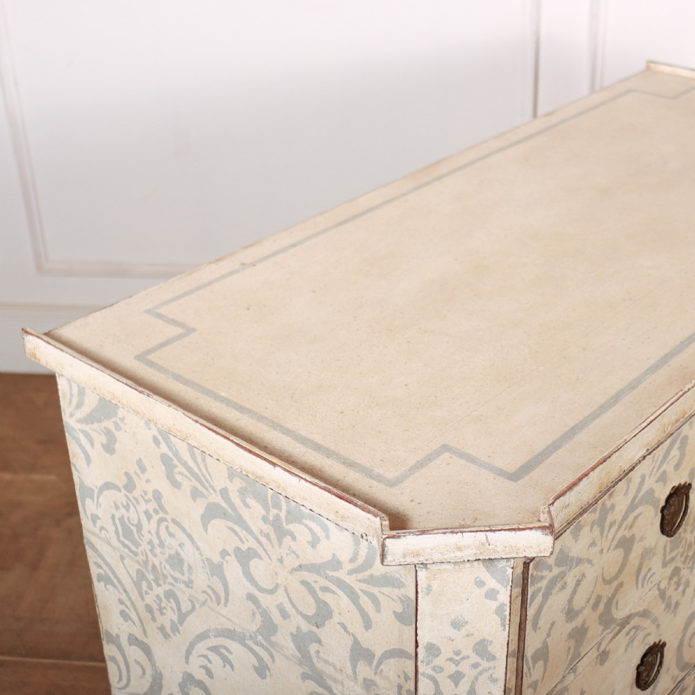 A Swedish painted pine commode featuring three drawers decorated with off-white and grey damask pattern paintwork, brass escutcheons, and tapered square legs. View X