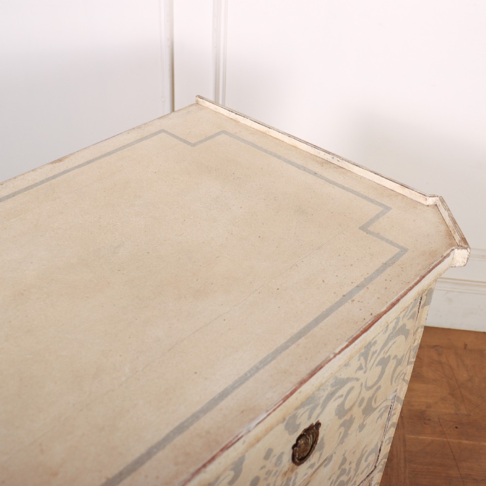 A Swedish painted pine commode featuring three drawers decorated with off-white and grey damask pattern paintwork, brass escutcheons, and tapered square legs. View XI