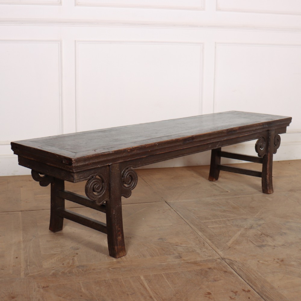 An antique dark brown elm low table featuring an inset panel top, straight legs with transverse stretchers, and carved scroll spandrels.