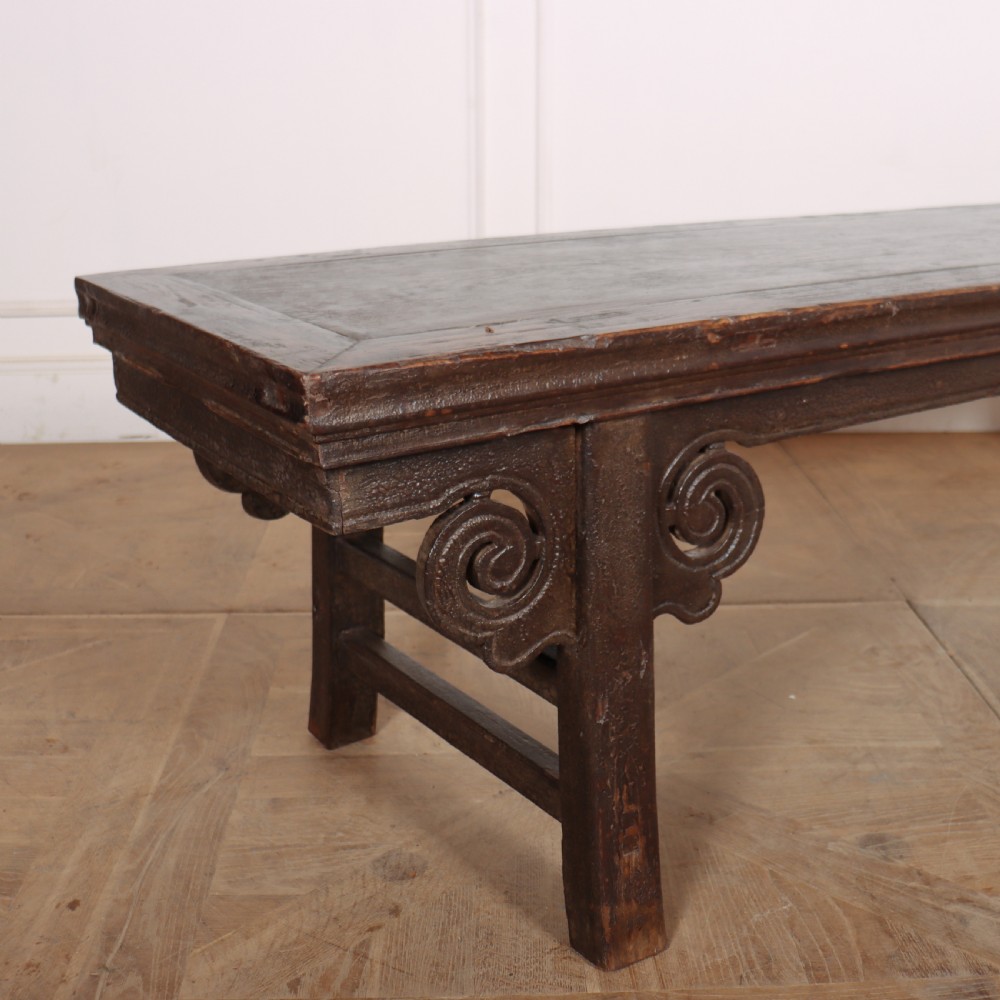 An antique dark brown elm low table featuring an inset panel top, straight legs with transverse stretchers, and carved scroll spandrels. View II