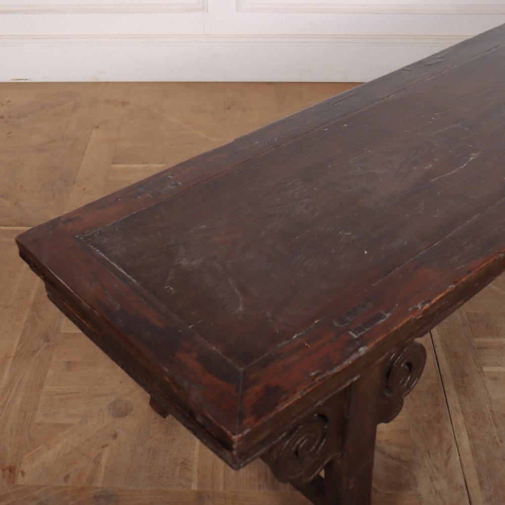 An antique dark brown elm low table featuring an inset panel top, straight legs with transverse stretchers, and carved scroll spandrels. View III