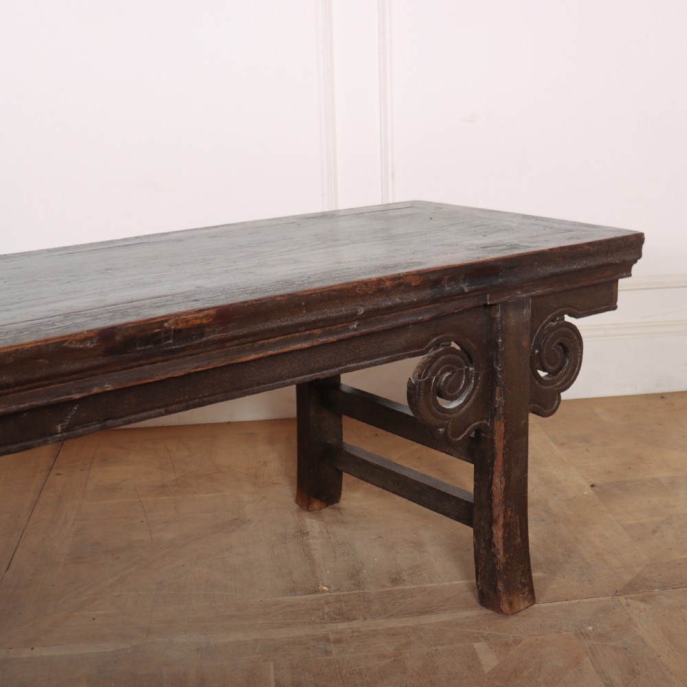 An antique dark brown elm low table featuring an inset panel top, straight legs with transverse stretchers, and carved scroll spandrels. View IV