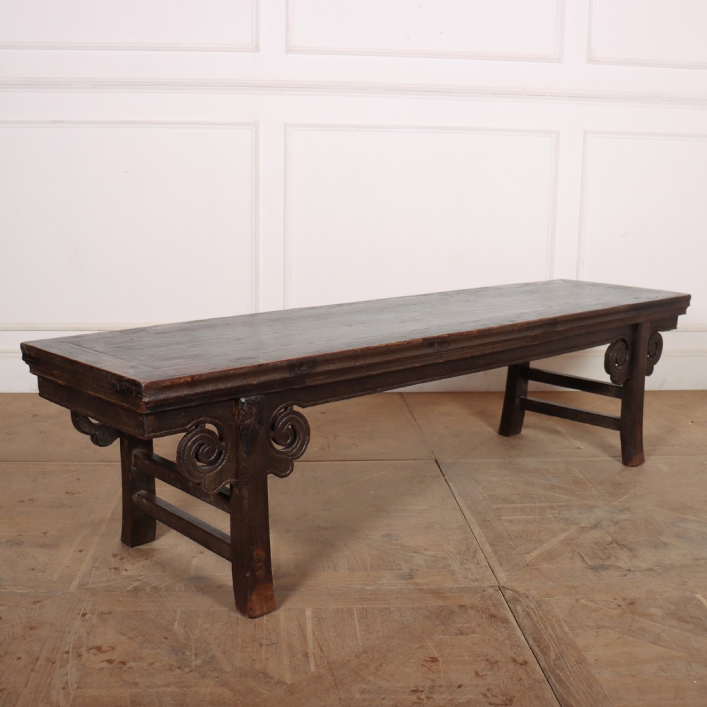 An antique dark brown elm low table featuring an inset panel top, straight legs with transverse stretchers, and carved scroll spandrels. View VI