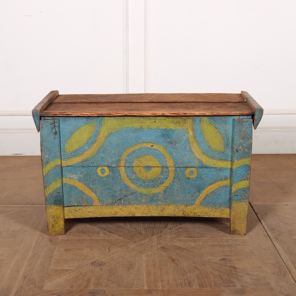 A rustic wooden storage coffer featuring hand-carved geometric circles painted in blue and yellow with a natural pine hinged top.