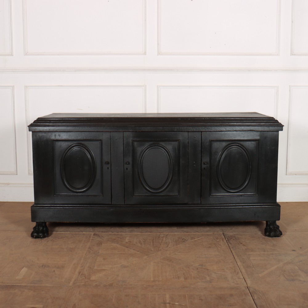 A low black painted wooden credenza featuring three panelled doors with oval mouldings and resting on carved paw feet.