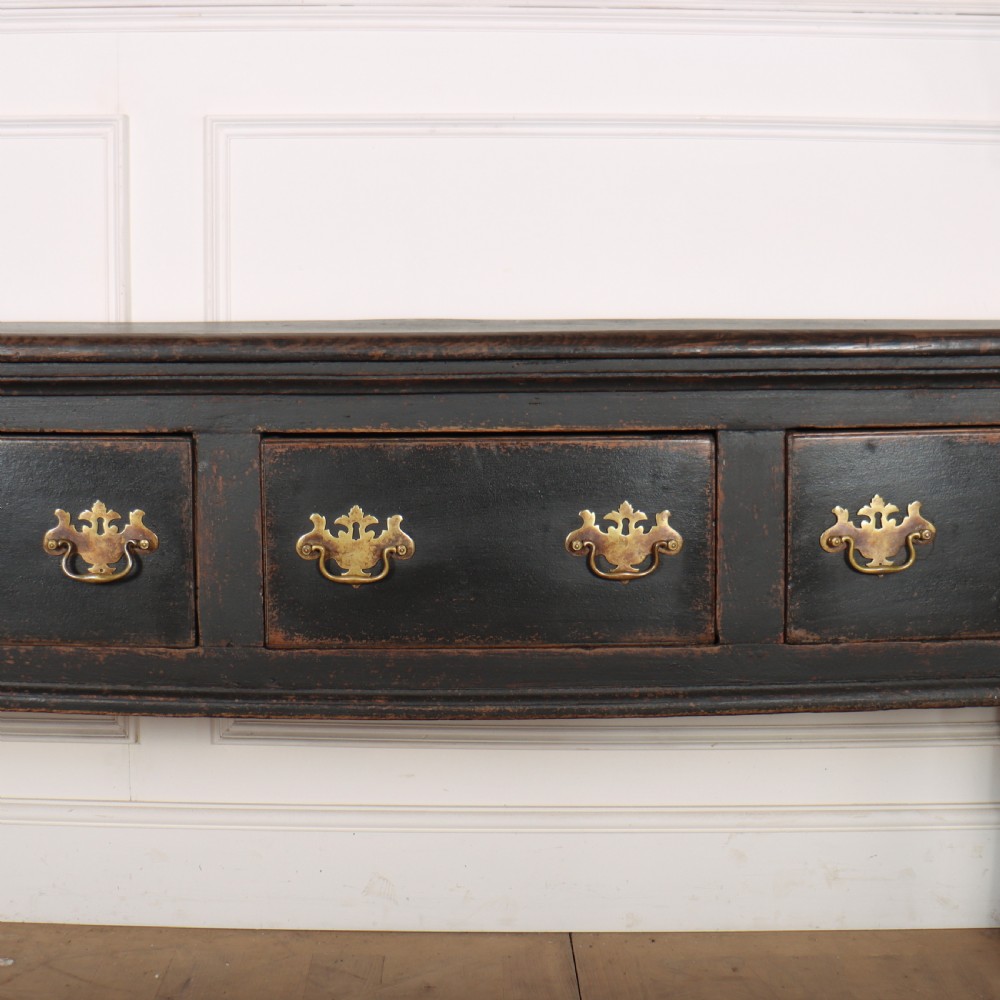 An 18th-century dark painted wooden kitchen dresser base featuring four drawers with brass handles beneath an open wall-mounted plate rack. View VII
