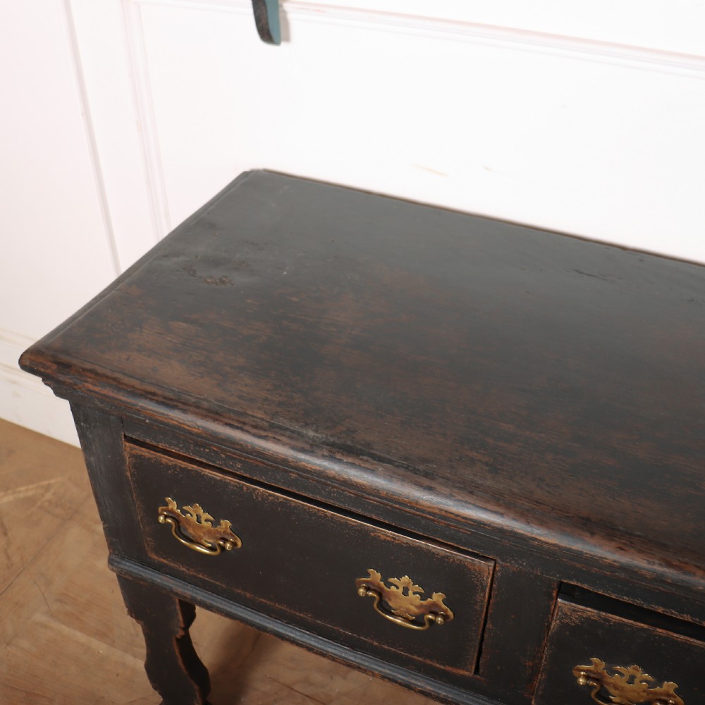 An 18th-century dark painted wooden kitchen dresser base featuring four drawers with brass handles beneath an open wall-mounted plate rack. View XI