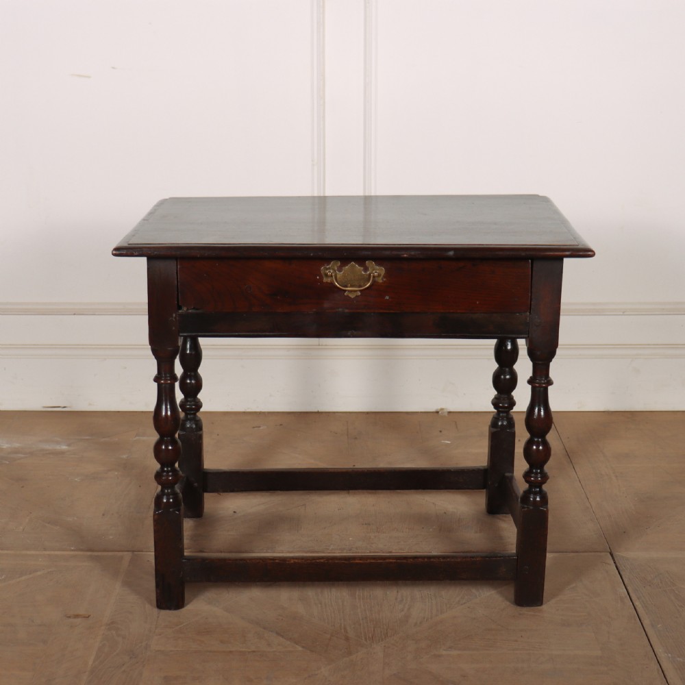 An 18th-century dark oak lamp table featuring turned legs, a single drawer with a brass handle, and low stretchers.
