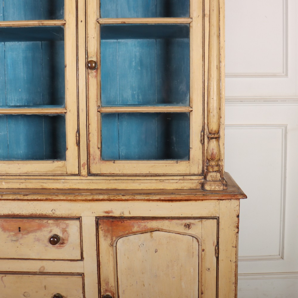 A cream painted timber kitchen dresser featuring a glazed three-door upper display cabinet with a vibrant blue interior above a base with drawers and panelled cupboard doors. View II