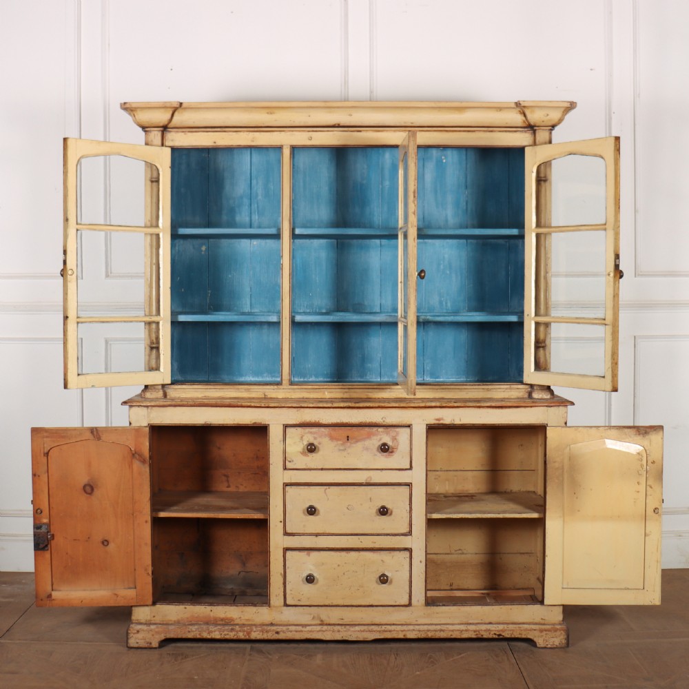 A cream painted timber kitchen dresser featuring a glazed three-door upper display cabinet with a vibrant blue interior above a base with drawers and panelled cupboard doors. View IV