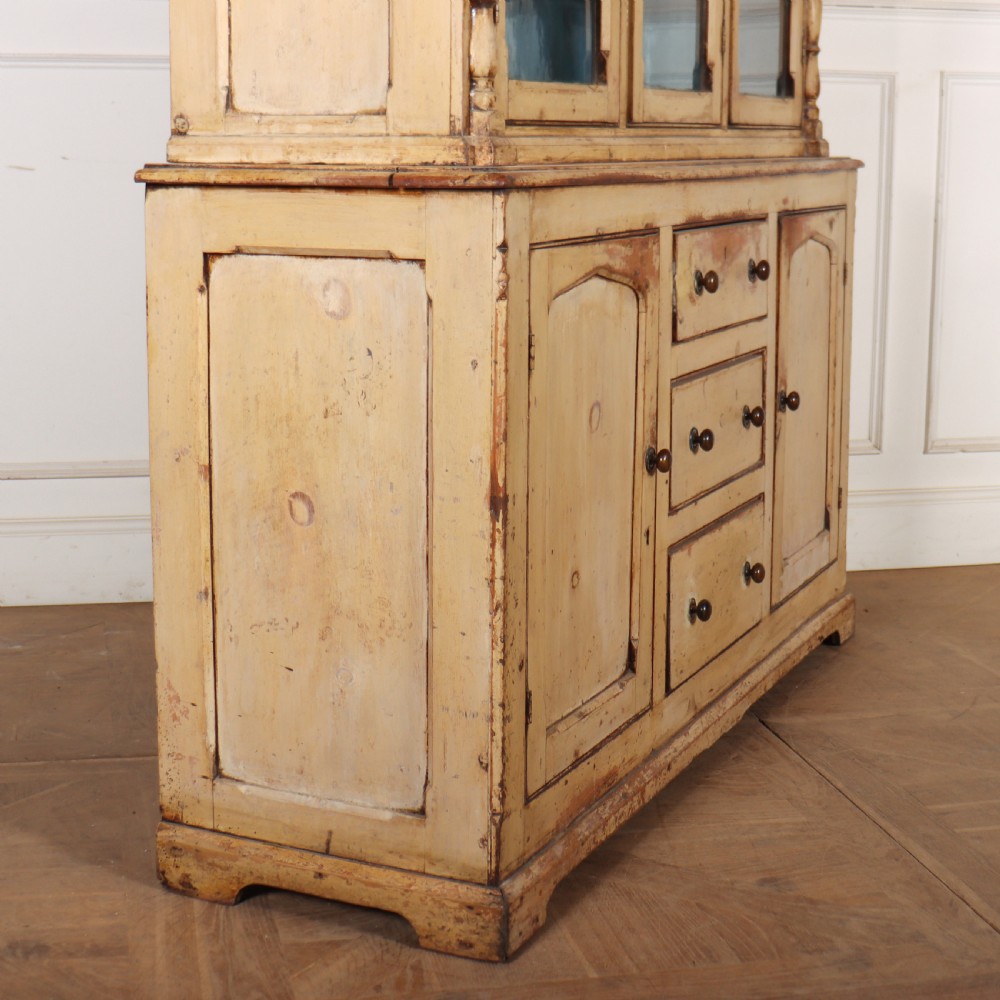A cream painted timber kitchen dresser featuring a glazed three-door upper display cabinet with a vibrant blue interior above a base with drawers and panelled cupboard doors. View VII