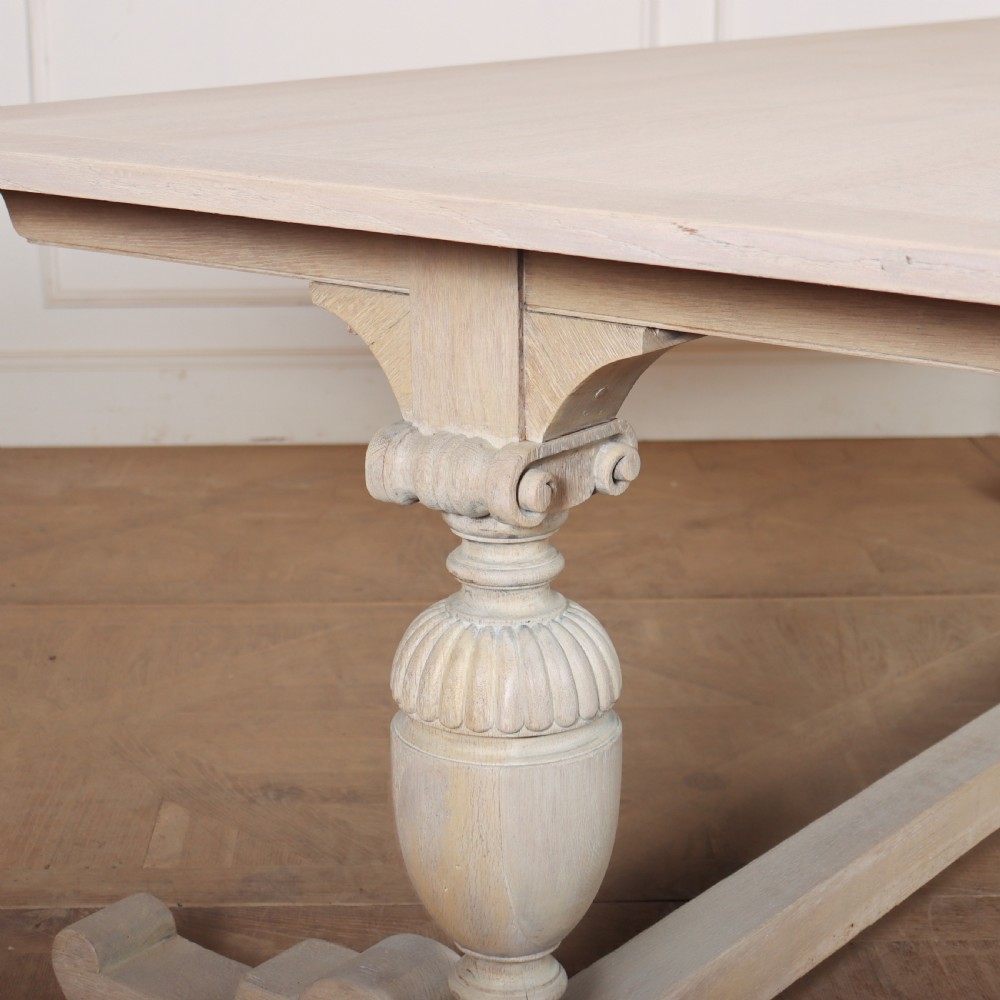 A long bleached oak dining table with a rectangular top and carved turned trestle base connected by a low central stretcher. View II