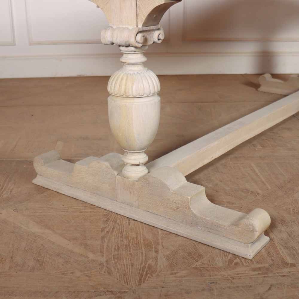 A long bleached oak dining table with a rectangular top and carved turned trestle base connected by a low central stretcher. View III