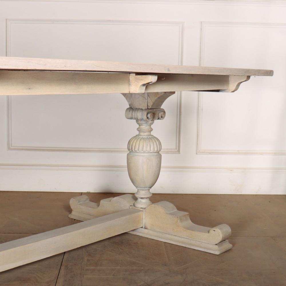 A long bleached oak dining table with a rectangular top and carved turned trestle base connected by a low central stretcher. View IV