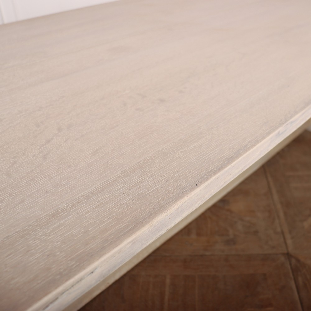 A long bleached oak dining table with a rectangular top and carved turned trestle base connected by a low central stretcher. View V