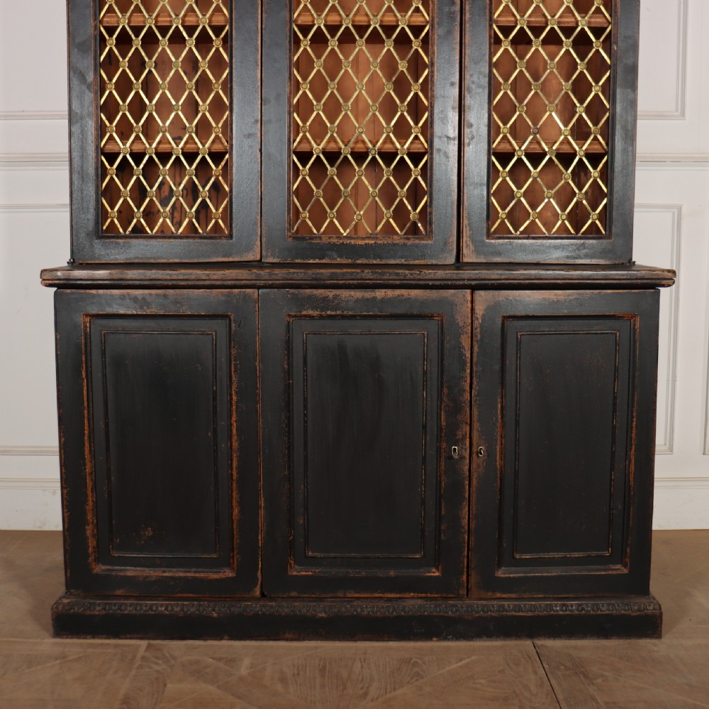 A tall black painted antique bookcase featuring three upper doors with gold-tone brass lattice grilles over three solid panelled lower cupboard doors. View II