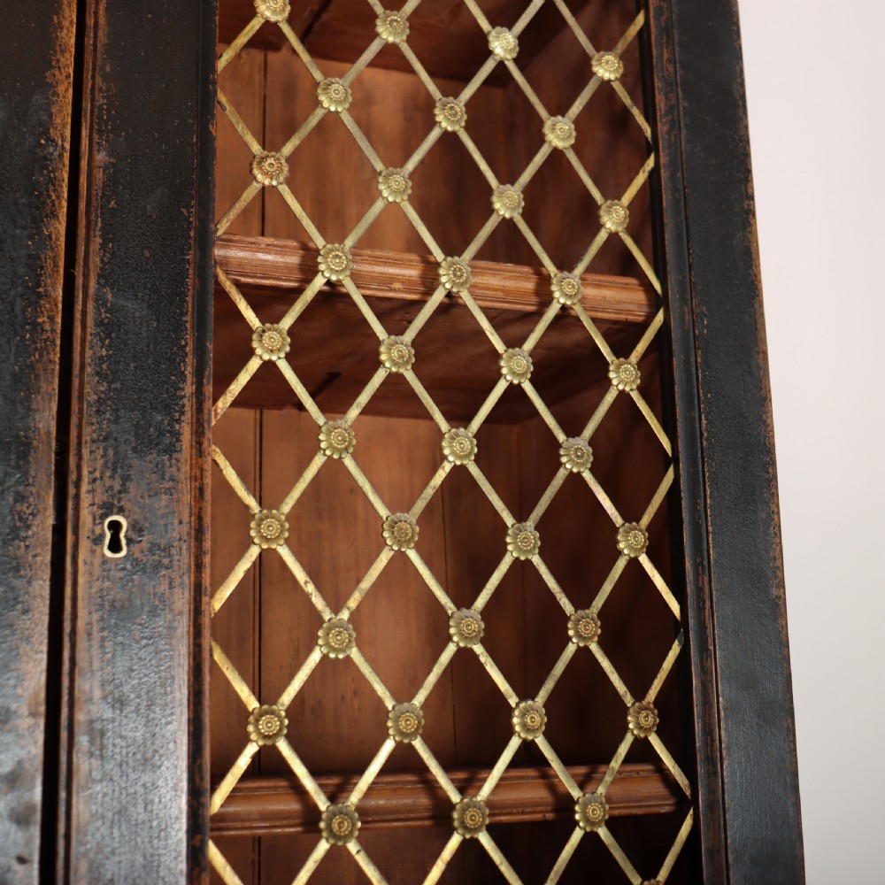 A tall black painted antique bookcase featuring three upper doors with gold-tone brass lattice grilles over three solid panelled lower cupboard doors. View V