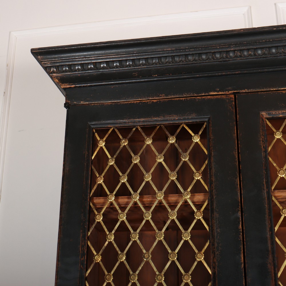 A tall black painted antique bookcase featuring three upper doors with gold-tone brass lattice grilles over three solid panelled lower cupboard doors. View VI