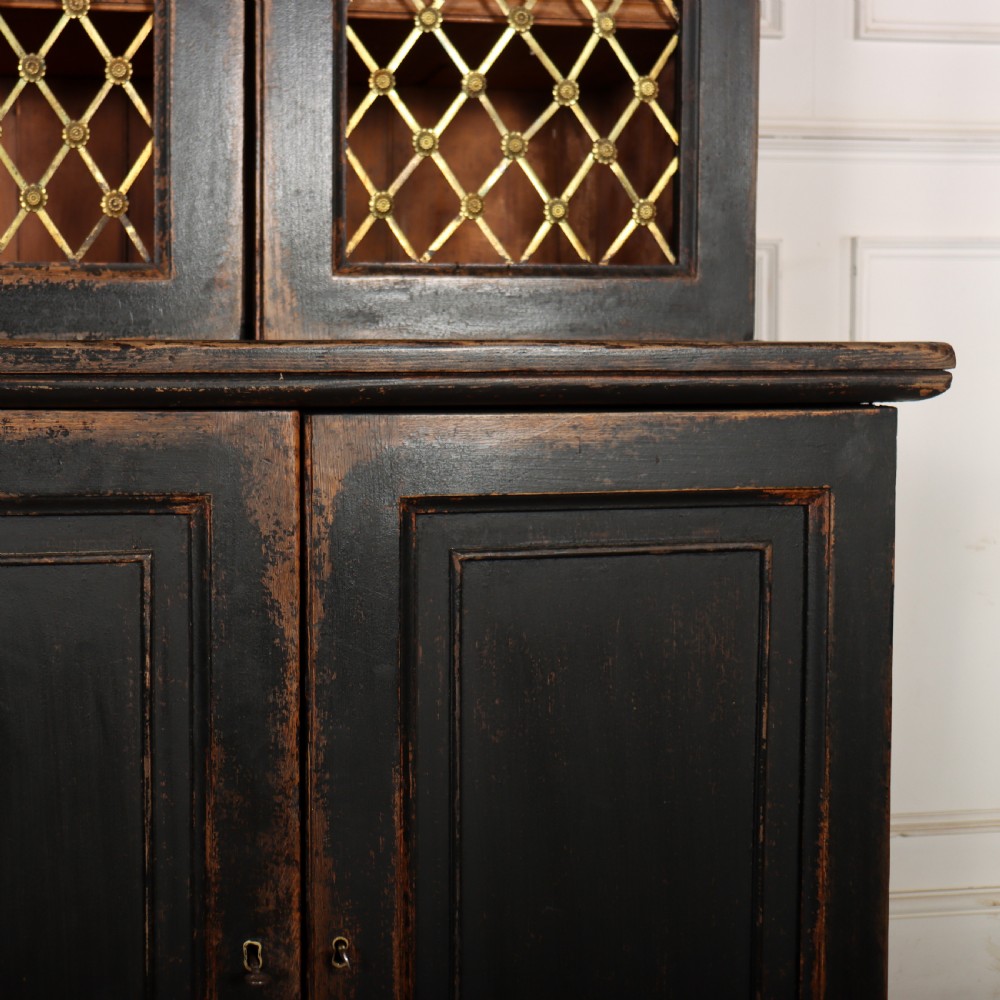 A tall black painted antique bookcase featuring three upper doors with gold-tone brass lattice grilles over three solid panelled lower cupboard doors. View VII