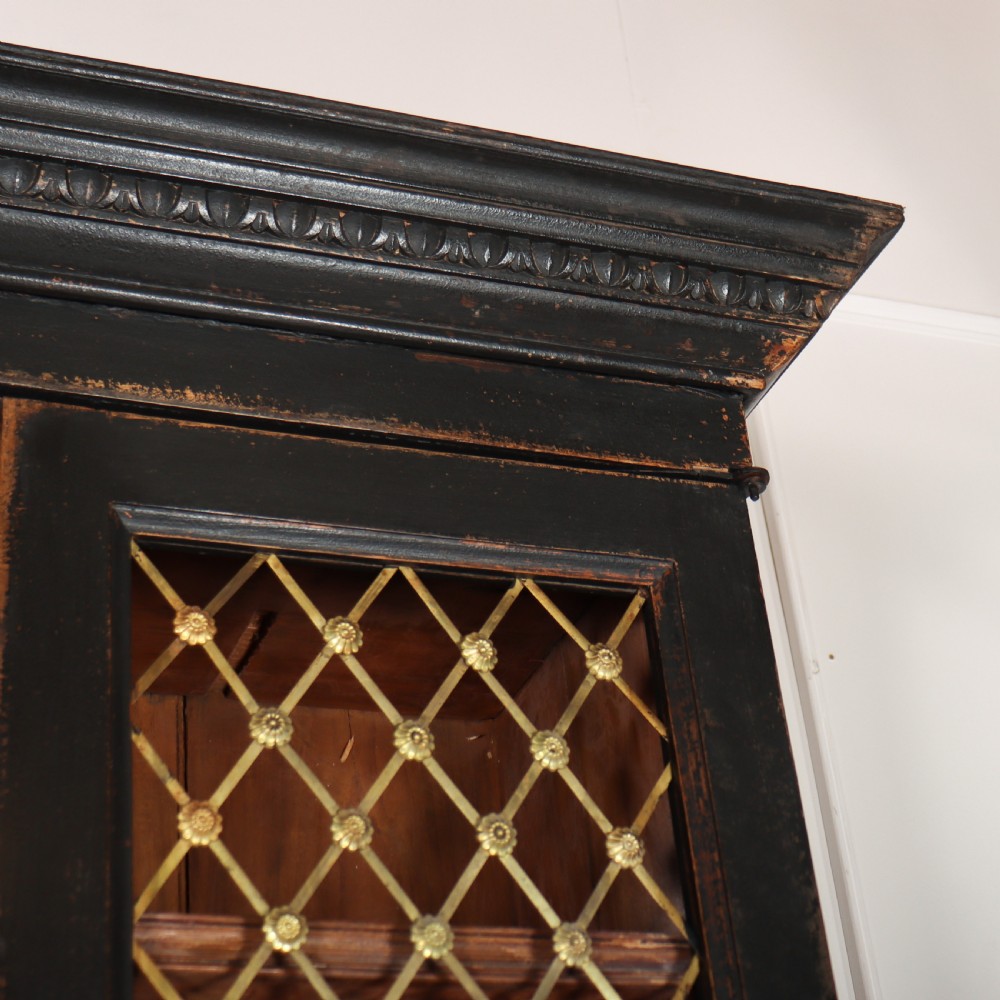 A tall black painted antique bookcase featuring three upper doors with gold-tone brass lattice grilles over three solid panelled lower cupboard doors. View VIII