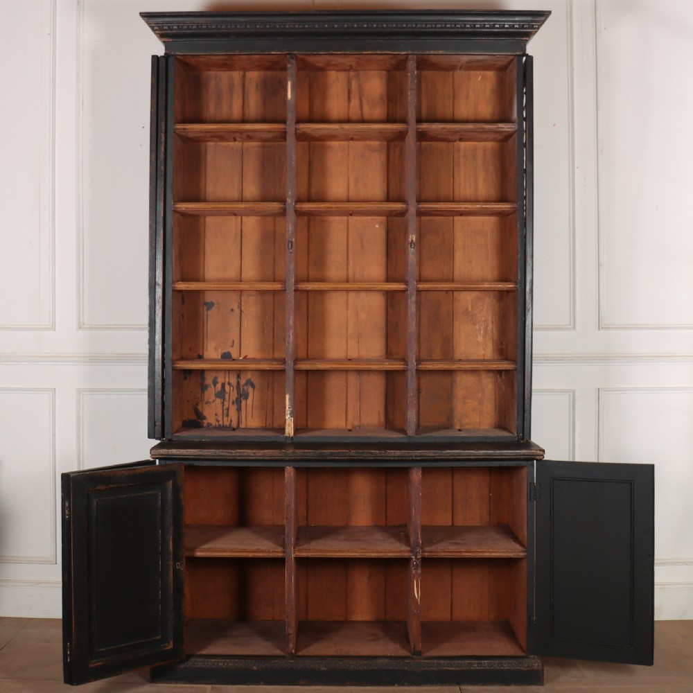 A tall black painted antique bookcase featuring three upper doors with gold-tone brass lattice grilles over three solid panelled lower cupboard doors. View IX