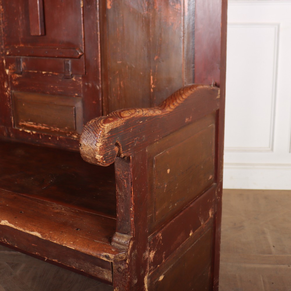 An 18th-century Spanish high-backed settle crafted from dark reddish-brown painted wood with raised back panels and integrated armrests. View II