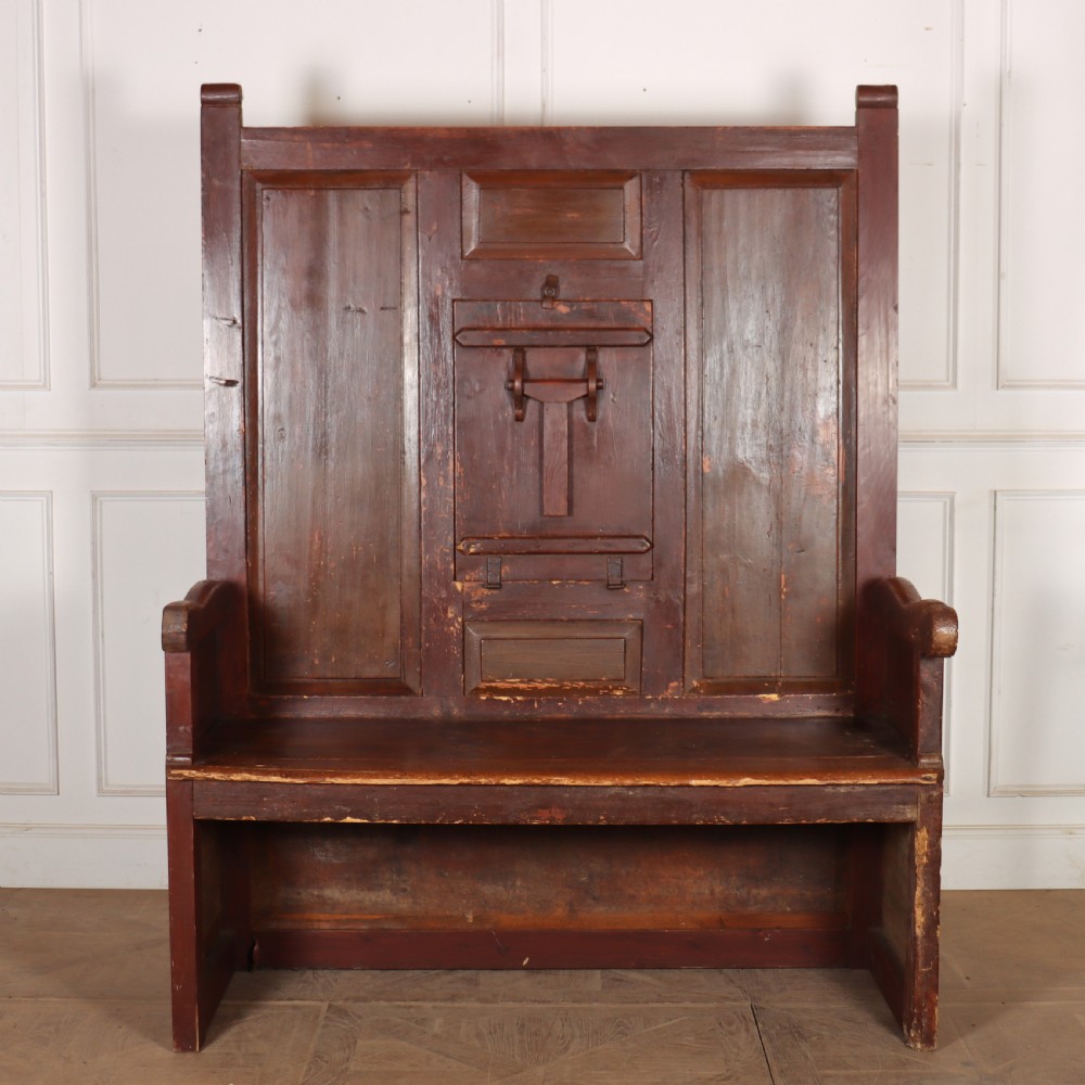 An 18th-century Spanish high-backed settle crafted from dark reddish-brown painted wood with raised back panels and integrated armrests.