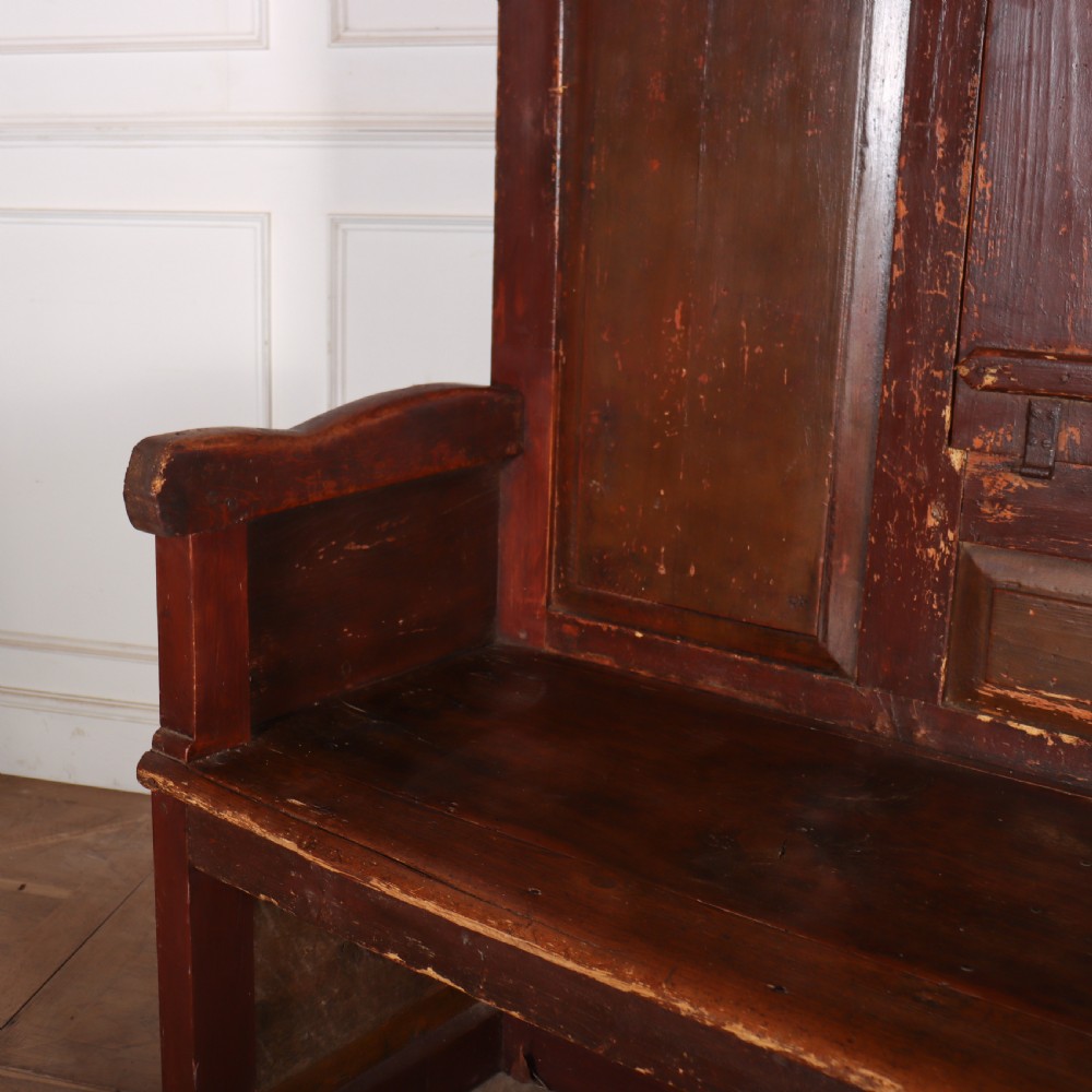 An 18th-century Spanish high-backed settle crafted from dark reddish-brown painted wood with raised back panels and integrated armrests. View III