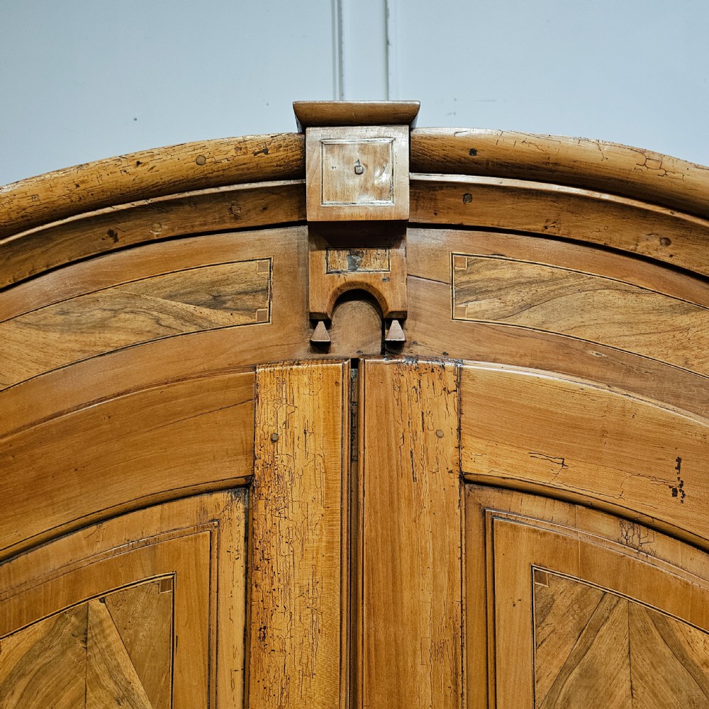 An 18th-century German pine armoire featuring an arched cornice, central cresting, geometric inlaid panel doors, and bun feet. View II