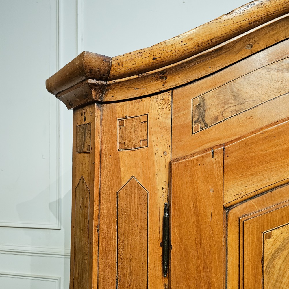 An 18th-century German pine armoire featuring an arched cornice, central cresting, geometric inlaid panel doors, and bun feet. View IV
