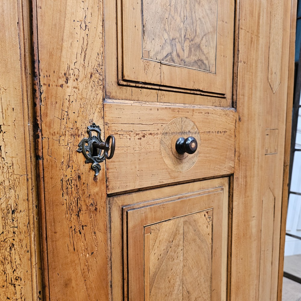 An 18th-century German pine armoire featuring an arched cornice, central cresting, geometric inlaid panel doors, and bun feet. View V