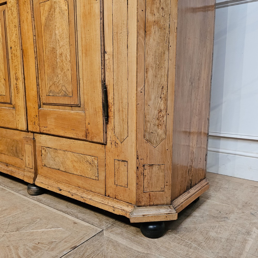An 18th-century German pine armoire featuring an arched cornice, central cresting, geometric inlaid panel doors, and bun feet. View VI