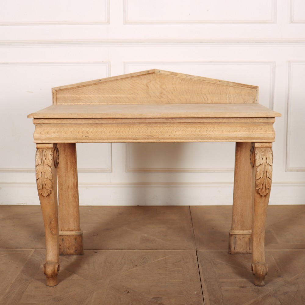 A light tan bleached oak console table with a low pedimented upstand and carved acanthus leaf front legs.