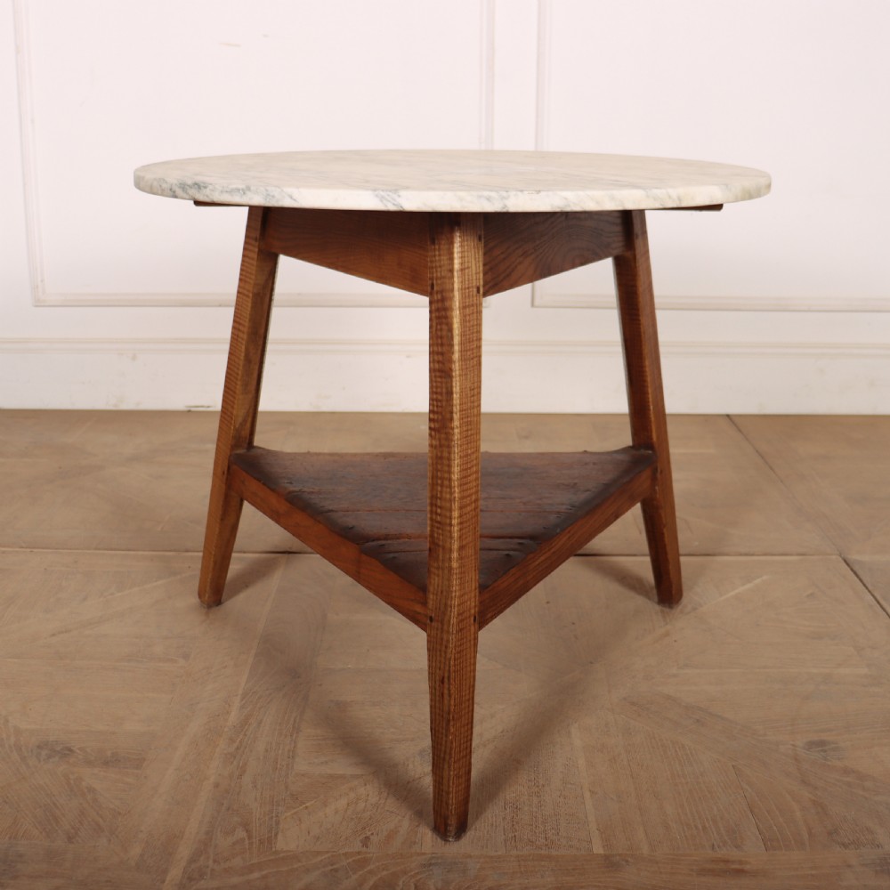 A nineteenth-century Welsh cricket table featuring a circular white marble top supported by a three-legged wooden frame with a lower triangular shelf.