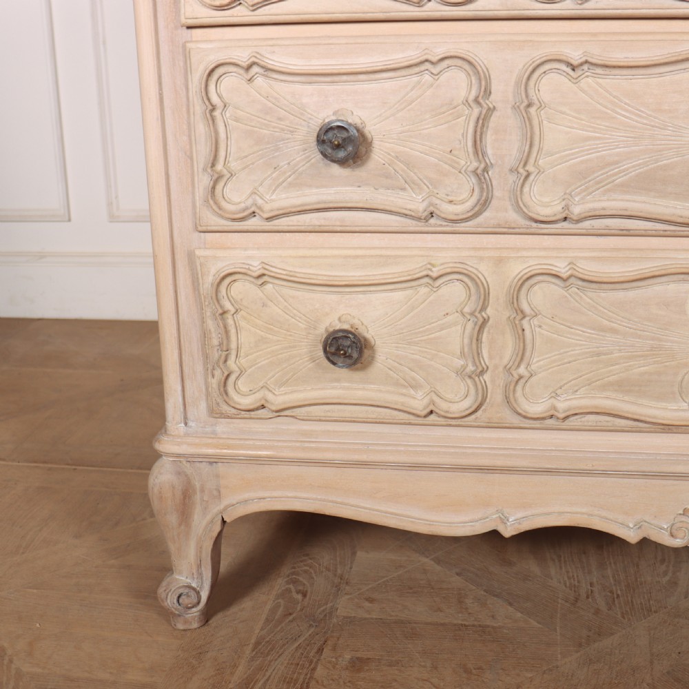 A French bleached oak commode featuring three carved panel drawers with dark metal handles, keyhole escutcheons, a black marble top, and cabriole feet. View III