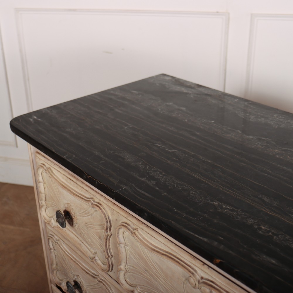 A French bleached oak commode featuring three carved panel drawers with dark metal handles, keyhole escutcheons, a black marble top, and cabriole feet. View X