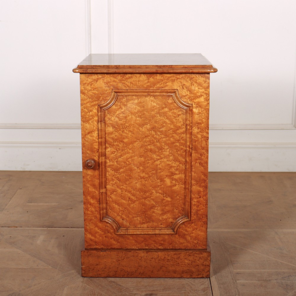 A golden brown burr elm bedside cabinet featuring a single panelled cupboard door and a solid plinth base.
