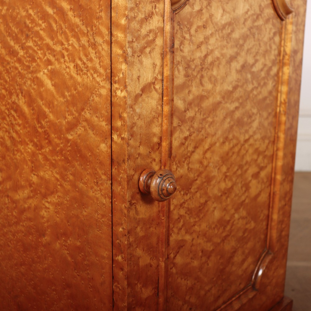 A golden brown burr elm bedside cabinet featuring a single panelled cupboard door and a solid plinth base. View III